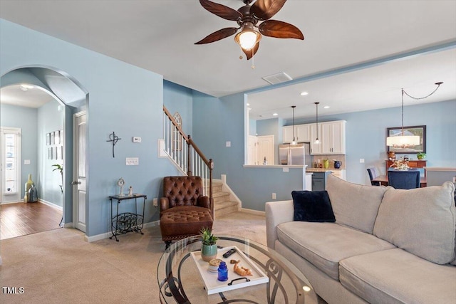 living room with arched walkways, light carpet, visible vents, baseboards, and stairway