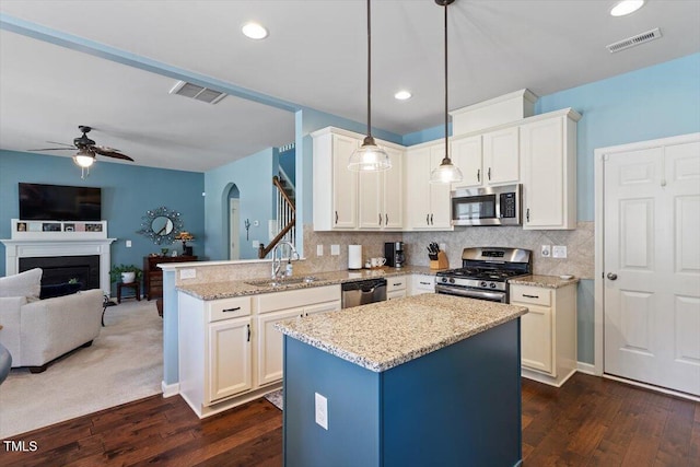 kitchen featuring visible vents, open floor plan, stainless steel appliances, pendant lighting, and a sink