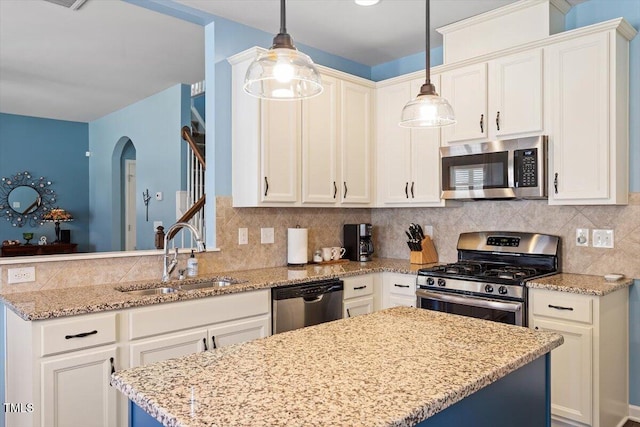 kitchen with decorative backsplash, appliances with stainless steel finishes, hanging light fixtures, light stone countertops, and a sink