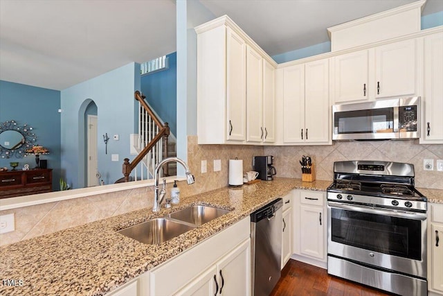 kitchen with tasteful backsplash, arched walkways, light stone counters, appliances with stainless steel finishes, and a sink