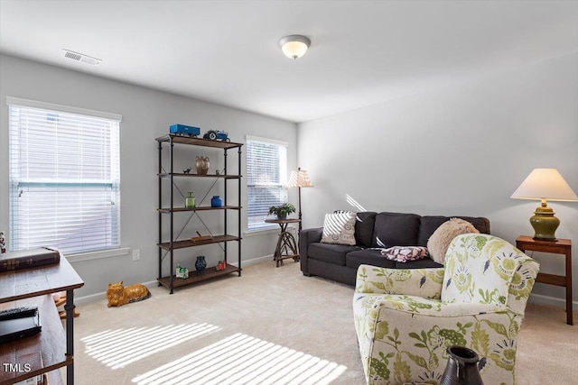 living area featuring baseboards, visible vents, and light colored carpet