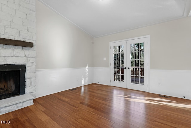 unfurnished living room featuring lofted ceiling, hardwood / wood-style floors, a stone fireplace, and french doors