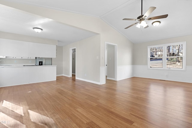 unfurnished living room with vaulted ceiling, ceiling fan, sink, and light wood-type flooring