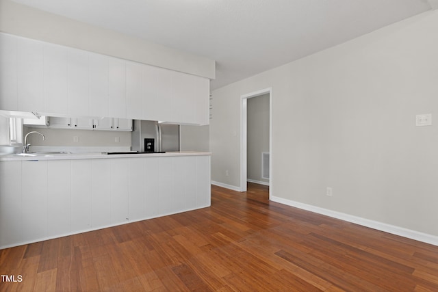 kitchen featuring white cabinetry, sink, stainless steel fridge, kitchen peninsula, and dark wood-type flooring