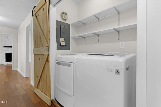 clothes washing area featuring a fireplace, wood-type flooring, electric panel, a barn door, and washer and clothes dryer