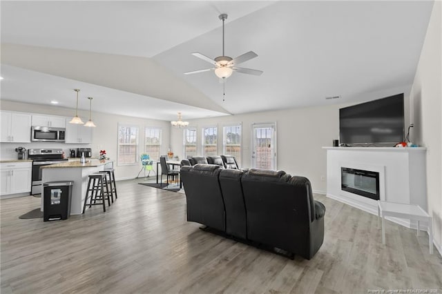 living room featuring lofted ceiling, ceiling fan with notable chandelier, and light hardwood / wood-style floors