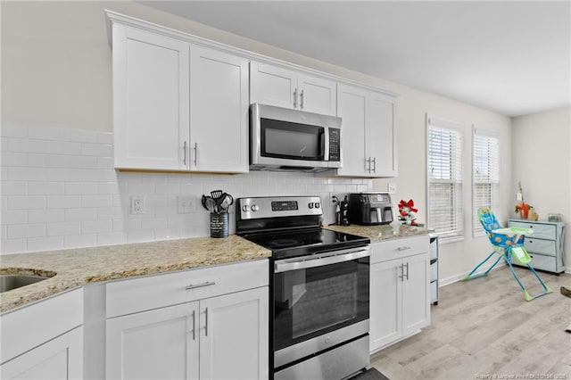 kitchen with backsplash, stainless steel appliances, light hardwood / wood-style floors, light stone countertops, and white cabinets