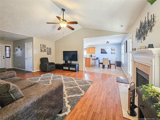 living room featuring vaulted ceiling, hardwood / wood-style floors, ceiling fan, a high end fireplace, and a textured ceiling