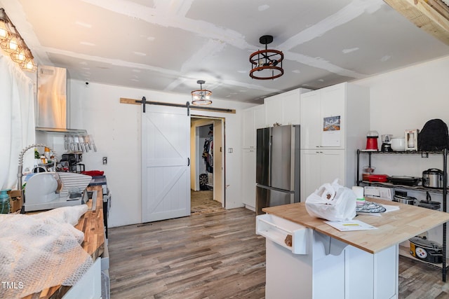 kitchen with stainless steel refrigerator, a barn door, hardwood / wood-style floors, and white cabinets