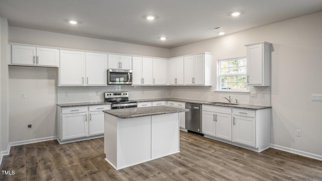 kitchen with white cabinetry, stainless steel appliances, dark hardwood / wood-style floors, a kitchen island, and dark stone counters