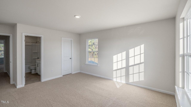 unfurnished bedroom with connected bathroom, carpet flooring, and multiple windows