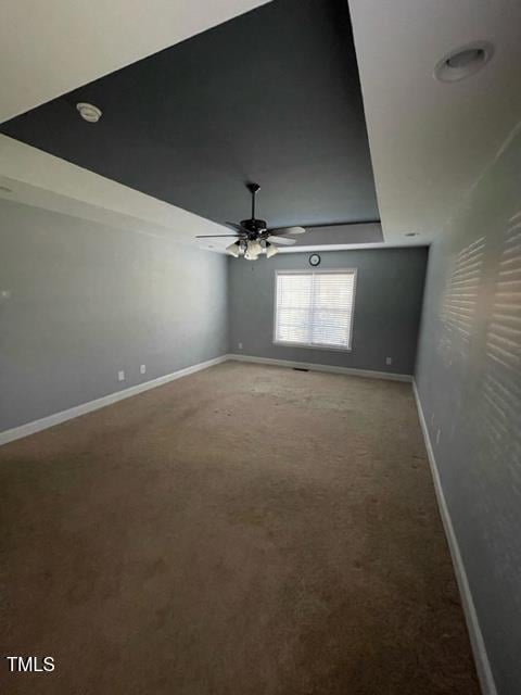 carpeted spare room featuring a raised ceiling and ceiling fan