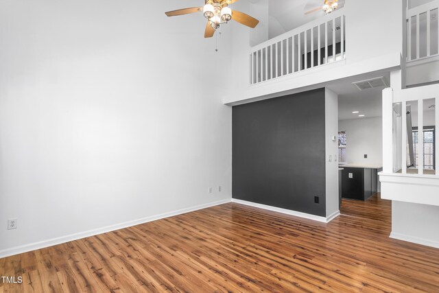empty room with a high ceiling, ceiling fan, and dark hardwood / wood-style flooring