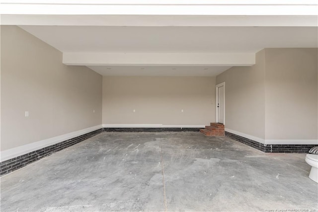 unfurnished room featuring unfinished concrete flooring, beam ceiling, and baseboards
