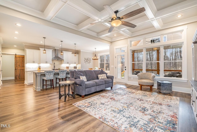 living room with beam ceiling, ceiling fan with notable chandelier, coffered ceiling, and a barn door