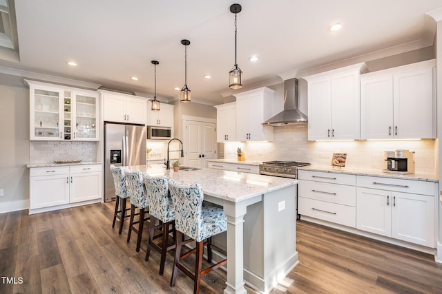 kitchen with pendant lighting, an island with sink, white cabinets, stainless steel appliances, and wall chimney range hood