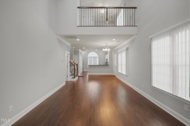 unfurnished living room featuring ornamental molding, dark wood-type flooring, an inviting chandelier, and a towering ceiling