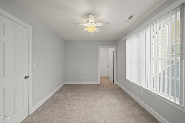 unfurnished bedroom featuring a walk in closet, light carpet, ceiling fan, and a closet