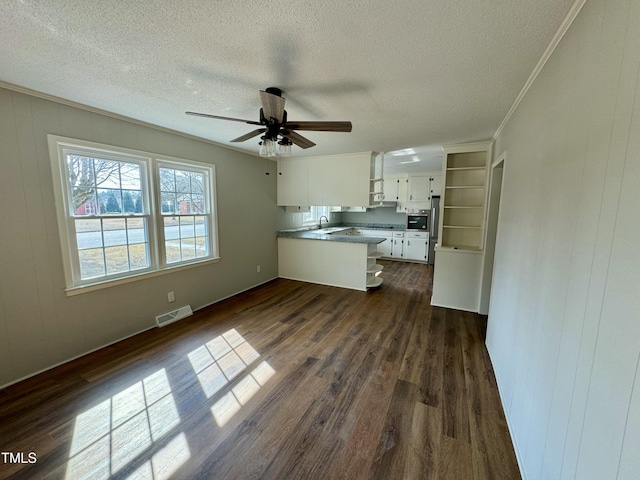 unfurnished living room with dark wood-type flooring, sink, a textured ceiling, ornamental molding, and ceiling fan