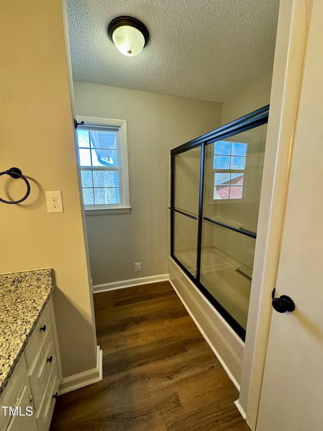 bathroom with vanity, wood-type flooring, shower / bath combination with glass door, and a textured ceiling