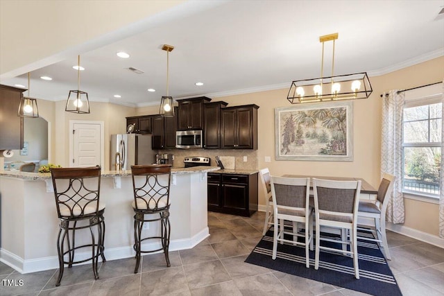 kitchen featuring a kitchen bar, light stone counters, decorative light fixtures, appliances with stainless steel finishes, and backsplash