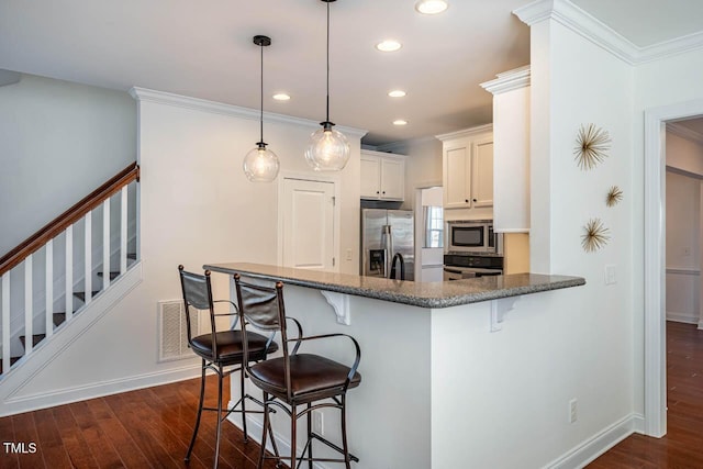 kitchen featuring appliances with stainless steel finishes, pendant lighting, white cabinets, a kitchen bar, and kitchen peninsula