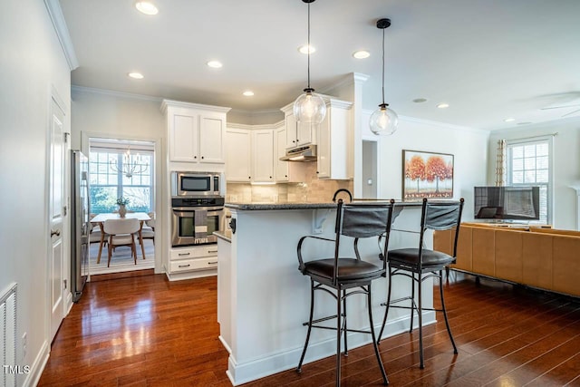 kitchen featuring pendant lighting, white cabinetry, stainless steel appliances, dark hardwood / wood-style floors, and dark stone counters