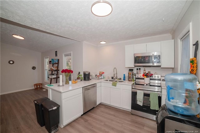 kitchen with sink, light hardwood / wood-style flooring, kitchen peninsula, stainless steel appliances, and white cabinets