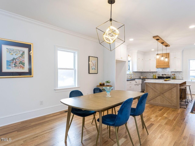 dining area featuring ornamental molding, sink, an inviting chandelier, and light hardwood / wood-style floors