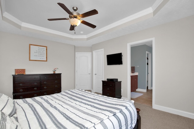 carpeted bedroom with ornamental molding, ensuite bathroom, ceiling fan, and a tray ceiling