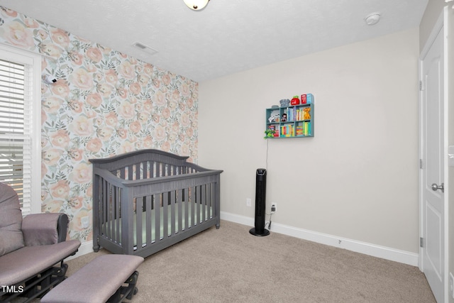 bedroom featuring a crib, light carpet, and a textured ceiling