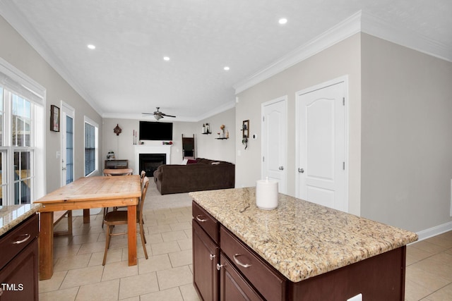 kitchen featuring light tile patterned flooring, ornamental molding, a center island, ceiling fan, and light stone counters