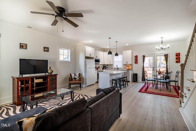 living room featuring sink, ceiling fan with notable chandelier, light hardwood / wood-style flooring, and french doors