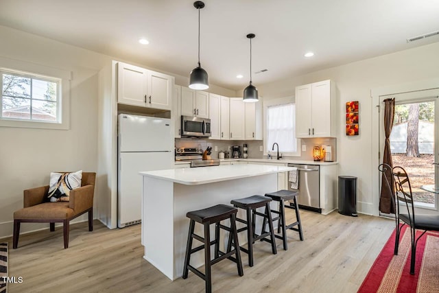 kitchen with sink, white cabinets, backsplash, stainless steel appliances, and light wood-type flooring