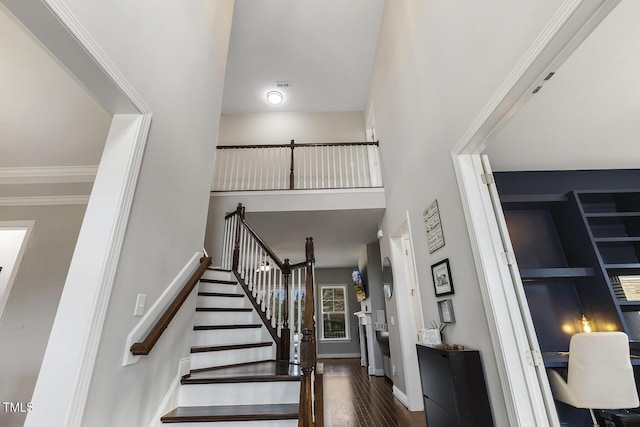 stairway featuring ornamental molding, a towering ceiling, and hardwood / wood-style floors