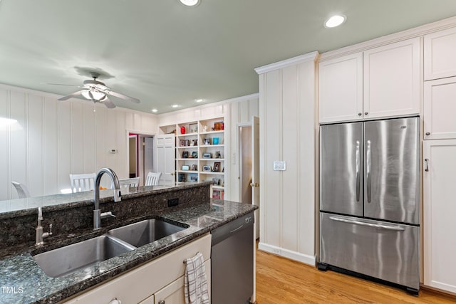 kitchen featuring appliances with stainless steel finishes, sink, dark stone countertops, white cabinets, and light wood-type flooring