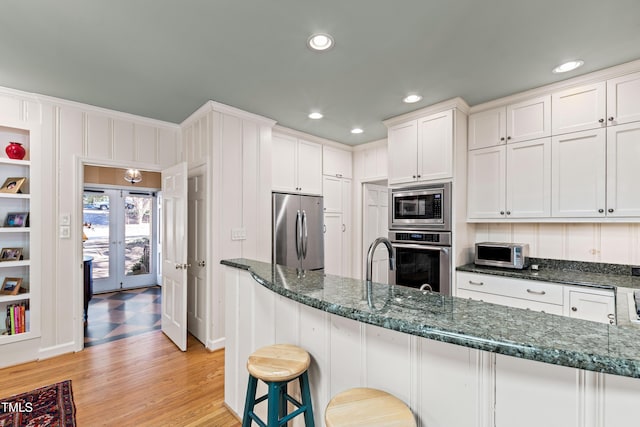 kitchen featuring white cabinetry, a kitchen breakfast bar, dark stone counters, and appliances with stainless steel finishes