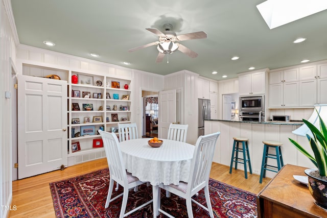 dining room featuring a skylight, ornamental molding, ceiling fan, and light hardwood / wood-style flooring