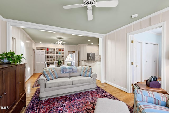 living room featuring built in features, ornamental molding, light hardwood / wood-style floors, and ceiling fan