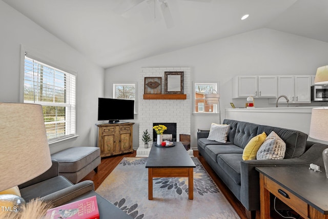 living room featuring lofted ceiling, sink, a brick fireplace, dark hardwood / wood-style floors, and ceiling fan