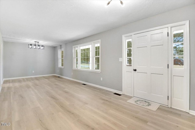 foyer entrance with an inviting chandelier, light hardwood / wood-style floors, and a textured ceiling