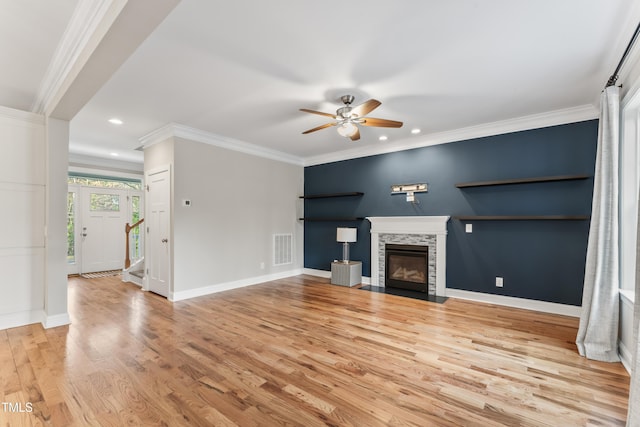 unfurnished living room featuring ceiling fan, ornamental molding, a stone fireplace, and light hardwood / wood-style flooring