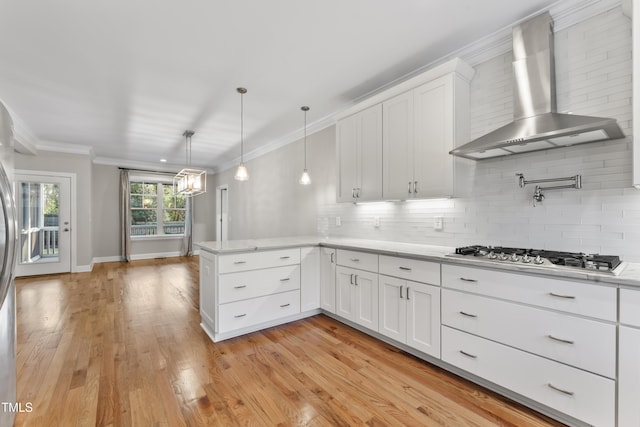 kitchen with pendant lighting, wall chimney range hood, kitchen peninsula, and white cabinets