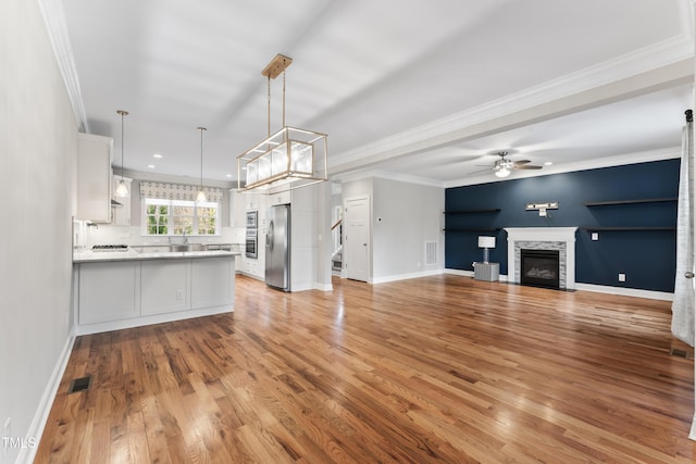 kitchen with a stone fireplace, pendant lighting, white cabinets, ornamental molding, and stainless steel refrigerator with ice dispenser