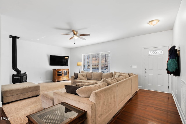 living room featuring dark wood-type flooring, ceiling fan, and a wood stove