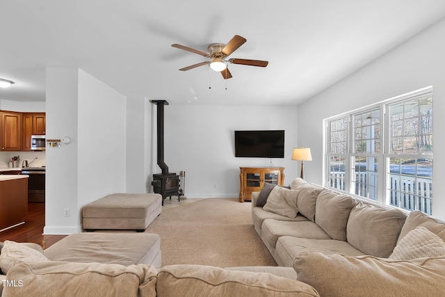 living room with a wood stove, light carpet, and ceiling fan