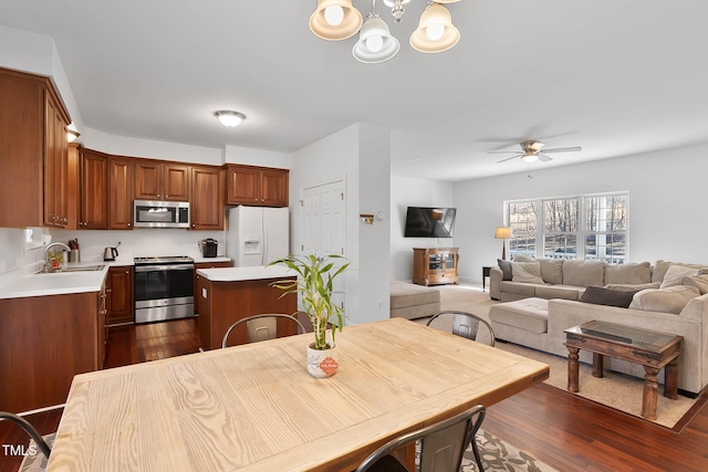 kitchen with sink, appliances with stainless steel finishes, dark hardwood / wood-style flooring, a kitchen island, and ceiling fan with notable chandelier