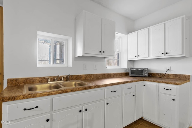 kitchen featuring dark tile patterned floors, white cabinetry, and sink