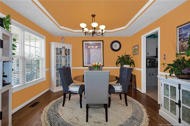 dining space with a tray ceiling, dark wood-type flooring, and a chandelier