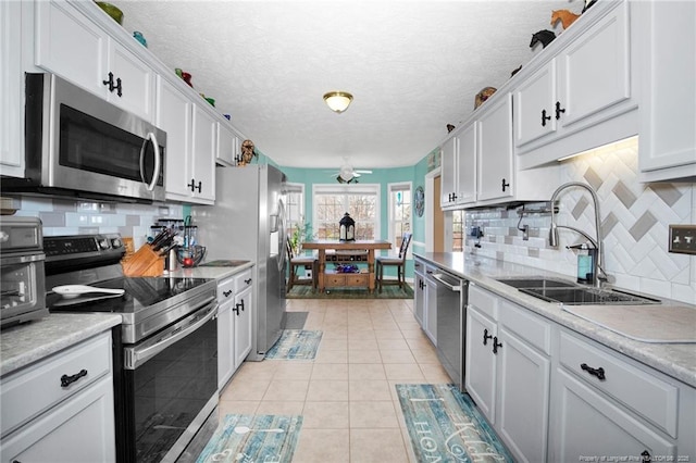 kitchen featuring tasteful backsplash, white cabinetry, sink, light tile patterned floors, and stainless steel appliances